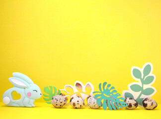 Frame for text with Easter bunny, quail eggs and leaves. Side view on yellow background Easter. Copyspace.