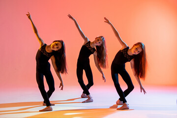group of three ballet girls in black tight-fitting suits dancing on red background with their long...