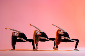 group of three ballet girls in black tight-fitting suits dancing on red background with their long...