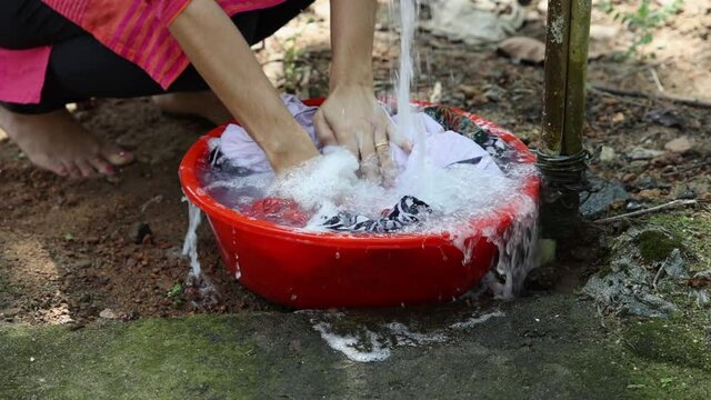 Women's hands wash dirty clothes in basin with detergent Kerala India Sri Lanka. Concept hand wash. Indian women female hand wash stain of dirty clothing with plastic scrub brush pipe water splashing