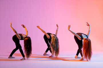 group of three girls in black tight-fitting suits dancing on red background with their long hair...