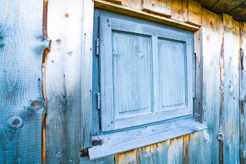 Small closed window in the wooden wall of an old house