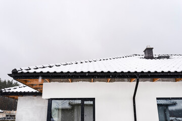 Single-family house roof covered with snow against a cloudy sky. Visible system chimney, roof...