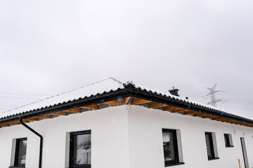 Single-family house roof covered with snow against a cloudy sky. Visible roof trusses, ventilation tile, windows and falling snow.
