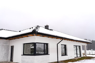 Single-family house roof covered with snow against a cloudy sky. Visible system chimney, doors, windows and falling snow.