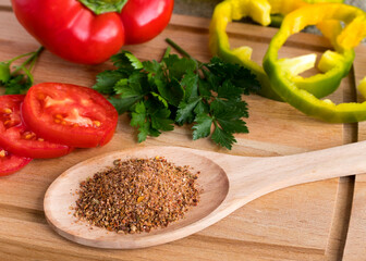 Spices on a spoon against the background of fresh vegetables tomatoes, paprika, parsley. Wooden background.