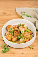Scallop baked with cauliflower in a plate with sauce on a light wooden background close-up.