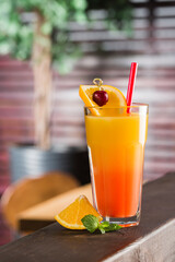 Tropical cocktail in a tall glass with a slice of orange and mint on the background of the restaurant interior.