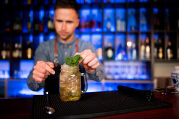Young guy a working as a bartender while preparing cocktails in a pub