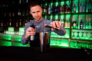 Young guy working as a bartender preparing cocktails in a pub