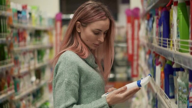 Blonde woman reads label of household products in supermarket