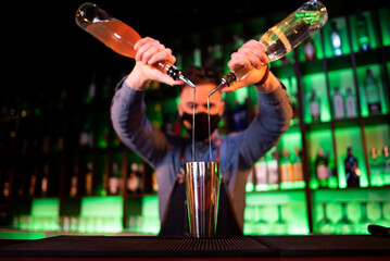 Young guy working as a bartender while preparing cocktails in a pub