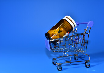 Shopping cart with pills in bottle. Medicine grade pharmaceutical tablets in mini shopping trolley. Medical pill for maintaining and improving health. Financial and economic concept