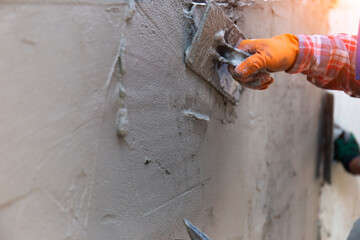 Worker hands that are plastering close-up, wear rubber gloves to prevent cement mortar to bite the wall for home construction and there is a beautiful orange light.