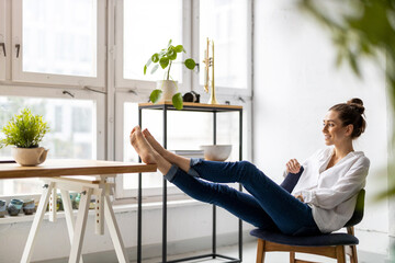 Young woman relaxing in office with her bare feet on desk 
