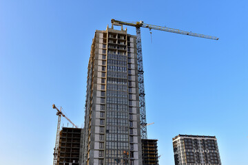 Fototapeta na wymiar Tower cranes in action at construction site. Crane the build the high-rise building. New residential skyscraper. Tall house renovation project, government programs