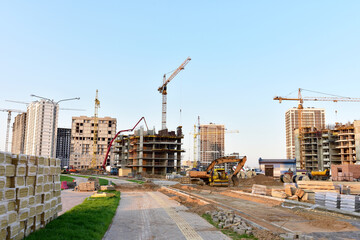 Tower cranes in action at construction site. Excavator on earthworks. Laying paving slabs and paving bricks. Screeding sand and road works. Pouring concrete from pump truck of ready-mixed truck