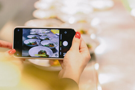 red nails female hand is taking pictures of served food on the buffet using her phone