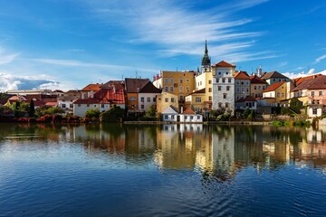 Fototapeta na wymiar Jindrichuv Hradec, Czech Republic - September 26 2019: View of the cityscape with historical buildings over the small Vajgar lake. Reflection in water. Bright sunny day with blue sky and clouds.