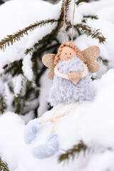 A soft textile doll with golden heart in hands sitting on the snow. Valentine’s Day, love, Merry Christmas, New Year concept.