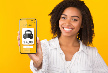 Black woman recommending mobile taxi service, showing smartphone with cab booking app on orange background