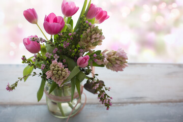 Composition with fresh spring flowers on gray wood, in background tender romantic pink bokeh with space for text. Short depth of field