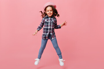 Adorable baby girl in fashionable street-style outfit jumps joyfully on pink background