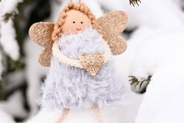 A soft textile doll with golden heart in hands sitting on the snow. Valentine’s Day, love, Merry Christmas, New Year concept.