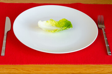 Diet lettuce leaf on plate with knife and fork on red tablecloth wooden table