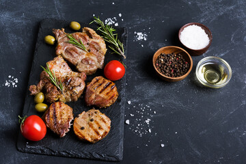  Variety of  grilled meat steaks steaks with spices, olives and tomatoes on black background.