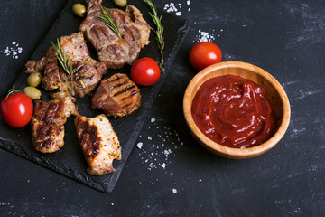  Variety of  grilled meat steaks steaks with spices, olives,  tomatoes  and sauce on black background.
