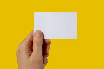 Human hand holds a blank sheet of paper on a yellow background with blank space for text, concept for business or training