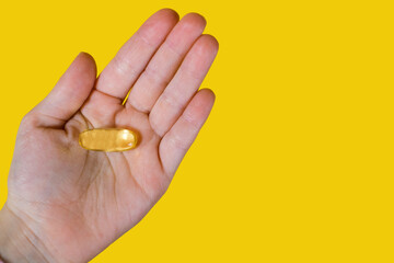 Capsules of fish oil in the palm of a person on a yellow background. A useful food supplement for improving heart function and blood clotting. Animal fat omega-3 omega-6