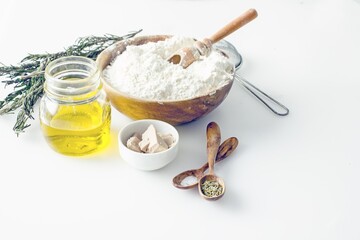 Ingredients for making Dough for focaccia or pizza. Flour, olive oil, yeast, seasonings, salt, herbs, greens close-up on a wooden table, copy space