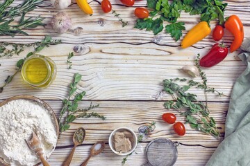 Ingredients for making Italian focaccia bread. Flour, olive oil, yeast, seasonings, salt, tomatoes, sweet herbs, greens close-up on a wooden table, copy space