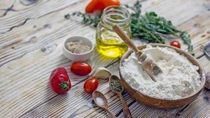 Ingredients for making Italian focaccia bread. Flour, olive oil, yeast, seasonings, salt, tomatoes, sweet herbs, greens close-up on a wooden table, copy space