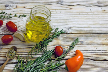 Olive oil in a glass jar and spicy herbs on a wooden table close-up, copy space. Home cooking, Italian recipes.
