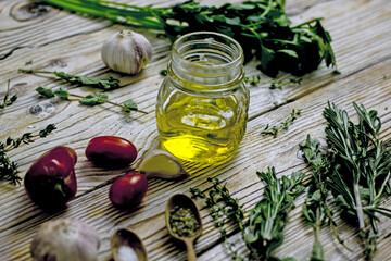 Olive oil in a glass jar and spicy herbs on a wooden table close-up, copy space. Home cooking, Italian recipes.