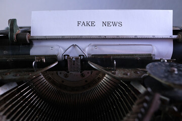 old typewriter on table, words fake news are printed on paper in large size, candle is burning, retro style, concept of information hoax in social media, misleading, exposing deception