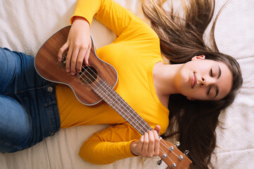 Fototapeta premium Young woman playing ukulele on top of bed