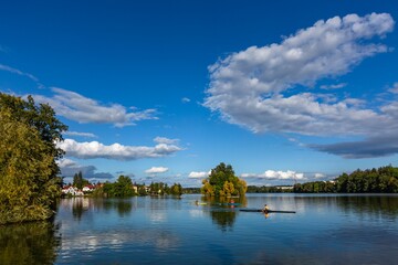 Fototapeta na wymiar Jindrichuv Hradec, Czech Republic - September 26 2019: View of the Vajgar lake and people kayaking. Reflection of the trees and bright blue sky with white clouds in the water. Sunny autumn day.