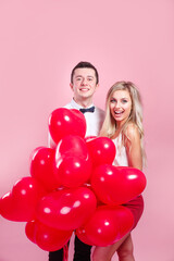 Fototapeta na wymiar Valentines day. Happy young couple with heart shaped balloons on pink background.
