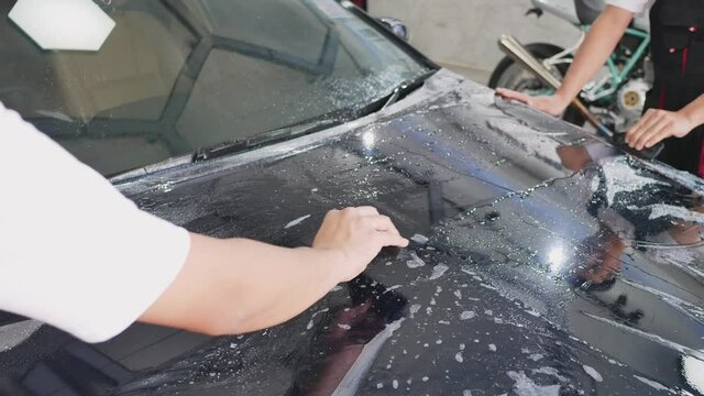 Mechanic with transparent film, car paint protection. Mechanic installs car paint protection film.