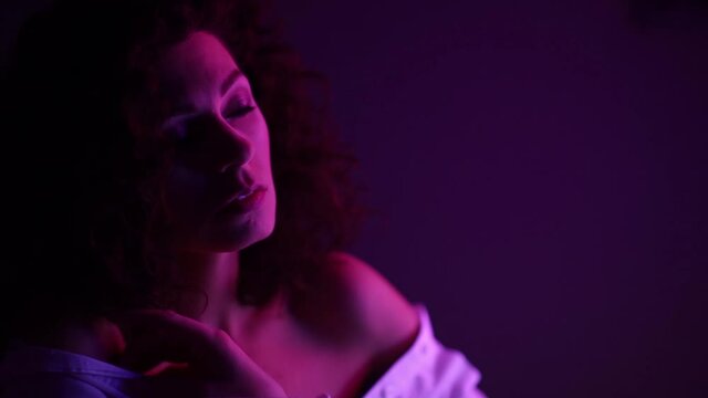 Fashion model curly woman in neon lights posing, light reflections on the skin