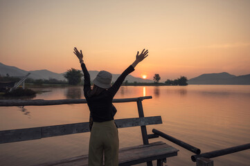 Fototapeta premium Beautiful young asian woman enjoying with sunrise on mountain lake at wooden pier