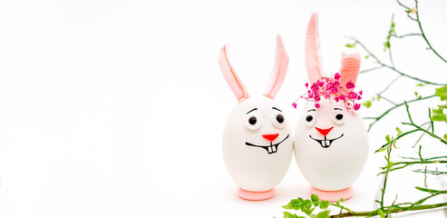 Creative Easter bunnies made of eggs with funny faces painted on them.White background,fresh flowers.Happy Easter concept.Copy space for text.