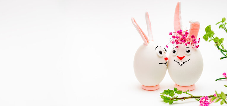 Creative Easter bunnies made of eggs with funny faces painted on them.White background,fresh flowers.Happy Easter concept.Copy space for text.