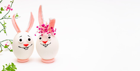 Creative Easter bunnies made of eggs with funny faces painted on them.White background,fresh flowers.Happy Easter concept.Copy space.