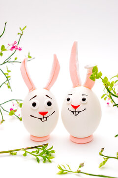 Happy Easter concept.Creative Easter bunnies made of eggs with funny faces painted on them.White background,fresh flowers.Copy space for text.