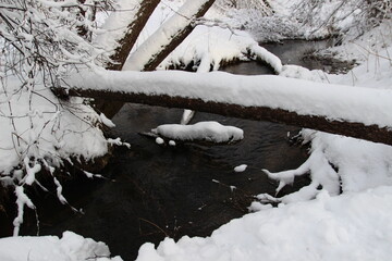 a stream in a winter snow-covered forest in the afternoon outside the city